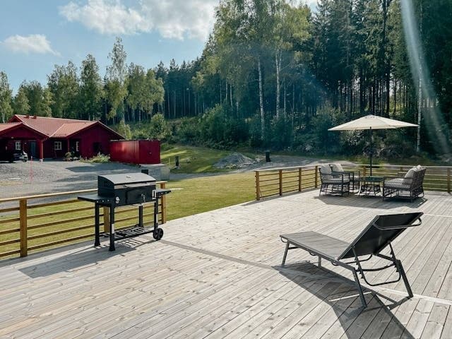 Rymlig terrass med trädäck, grillgrill och komfortabla loungestolar. Vacker utsikt över sjön och omgivande skog. Perfekt för avkoppling och matlagning utomhus.