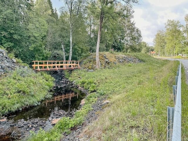 Vacker träbro över bäcken som slingrar sig genom fastighetens naturskön miljö. Omgiven av skog och grönska, perfekt för naturälskare.